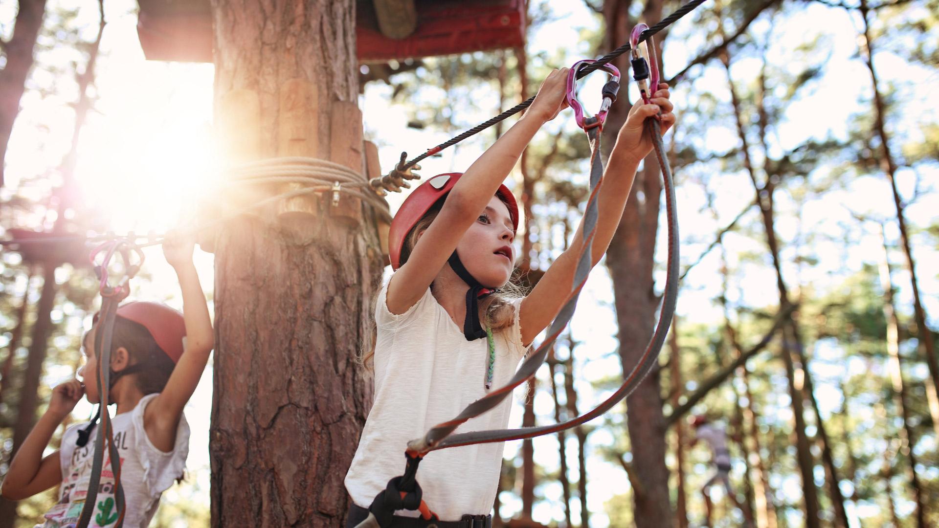 Bambina con casco rosso fa arrampicata sugli alberi in un parco avventura.