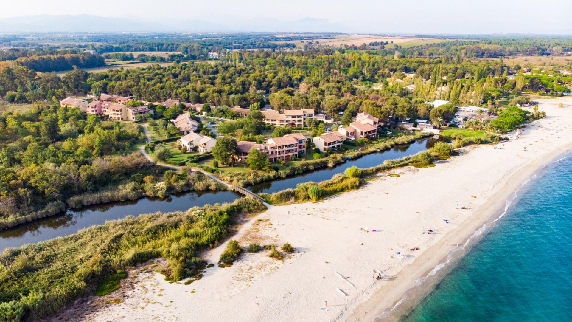 Vista aerea di un resort costiero immerso nella natura, vicino a una spiaggia sabbiosa.