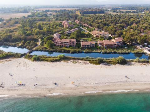 Spiaggia sabbiosa con mare turchese, circondata da villette e vegetazione lussureggiante.