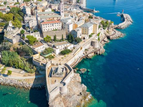 Vista aerea di una città costiera con fortificazioni storiche e mare cristallino.