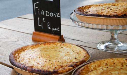 Torte Fiadone esposte su un tavolo di legno, prezzo indicato 4 euro per porzione.