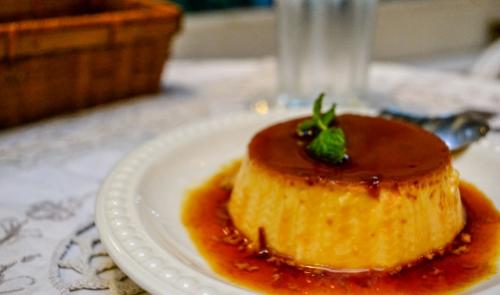 Crème caramel su piatto bianco, decorato con foglia di menta, su tovaglia ricamata.