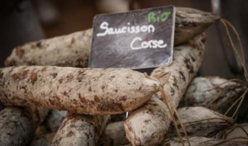 Salsicce corse biologiche esposte con etichetta in un mercato.