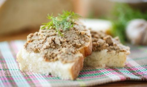 Fette di pane con paté, guarnite con erbe fresche su tovaglietta colorata.