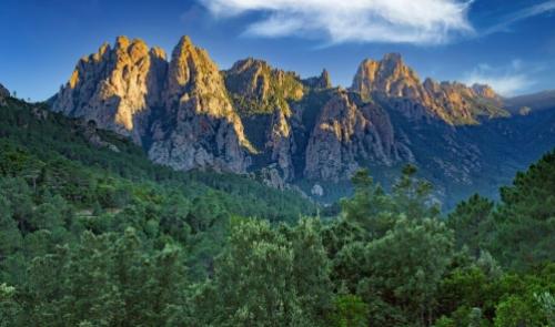 Montagne rocciose illuminate dal sole, circondate da una rigogliosa foresta verde.