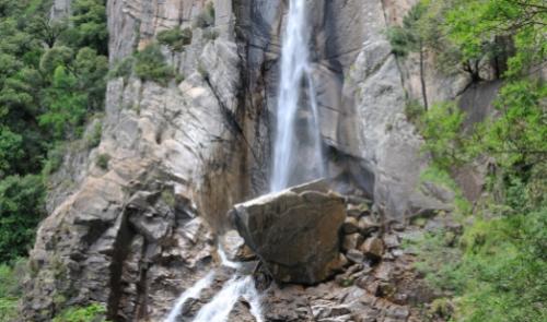 Cascata tra le rocce con vegetazione lussureggiante intorno.