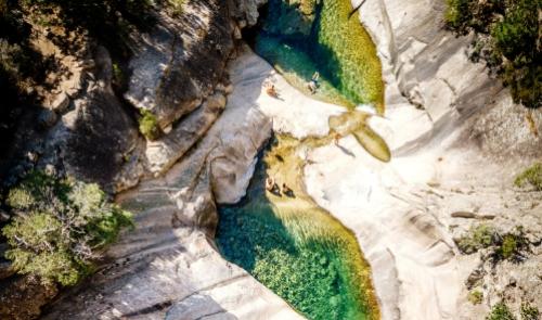 Piscine naturali tra rocce, con acqua cristallina e bagnanti immersi nel paesaggio.