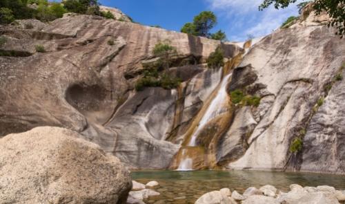 Cascata su rocce scoscese con piscina naturale e cielo azzurro.