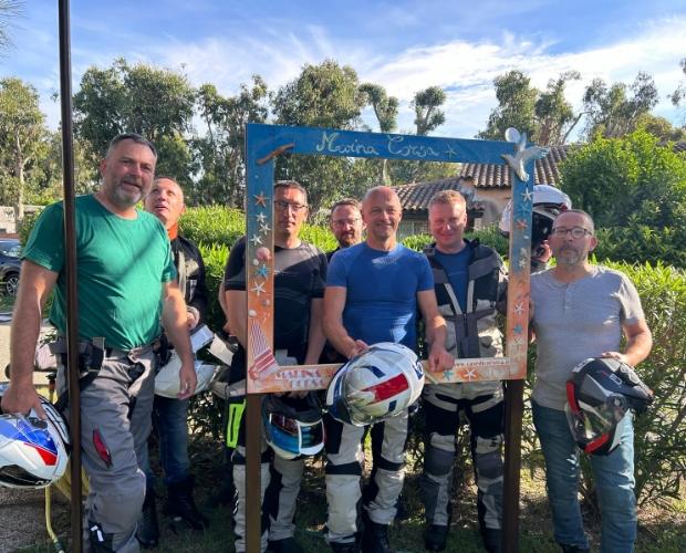 Gruppo di motociclisti posa con cornice decorativa all'aperto, tenendo i caschi in mano.