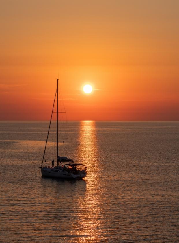 Barca a vela sul mare al tramonto con riflessi dorati sull'acqua.