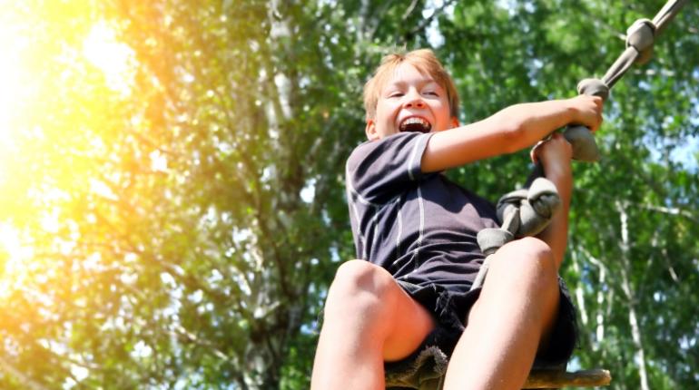 Bambino felice si diverte su una teleferica in un parco soleggiato.