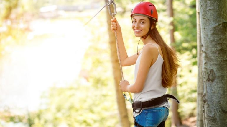 Donna sorridente su una zipline, indossa casco rosso e imbracatura di sicurezza.