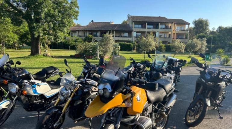 Moto parcheggiate all'aperto, con un edificio residenziale sullo sfondo e alberi intorno.