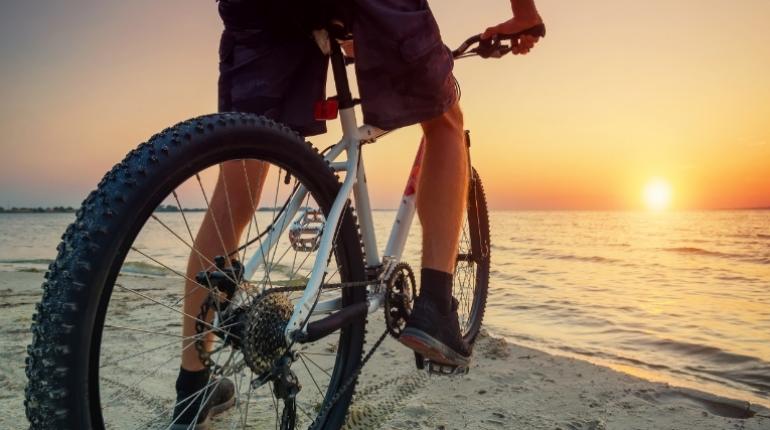 Ciclista sulla spiaggia al tramonto, pedalando lungo la riva del mare.
