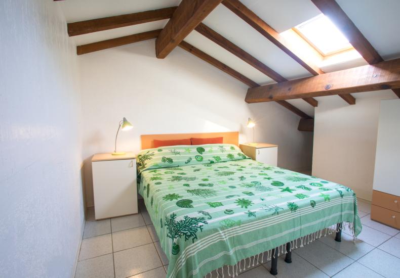 Camera da letto mansardata con letto matrimoniale e lucernario.