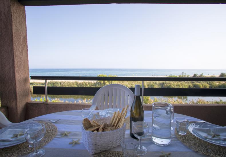Tavola apparecchiata con vista mare, bottiglia di vino e cestino di pane.