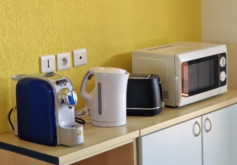 Elettrodomestici da cucina: macchina caffè, bollitore, tostapane e microonde su un piano.