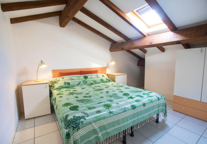 Camera da letto mansardata con letto matrimoniale e lucernario, arredamento semplice.