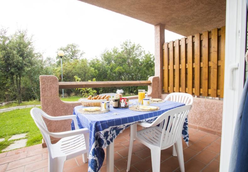 Terrazza con tavolo apparecchiato, sedie bianche, vista su giardino verde.