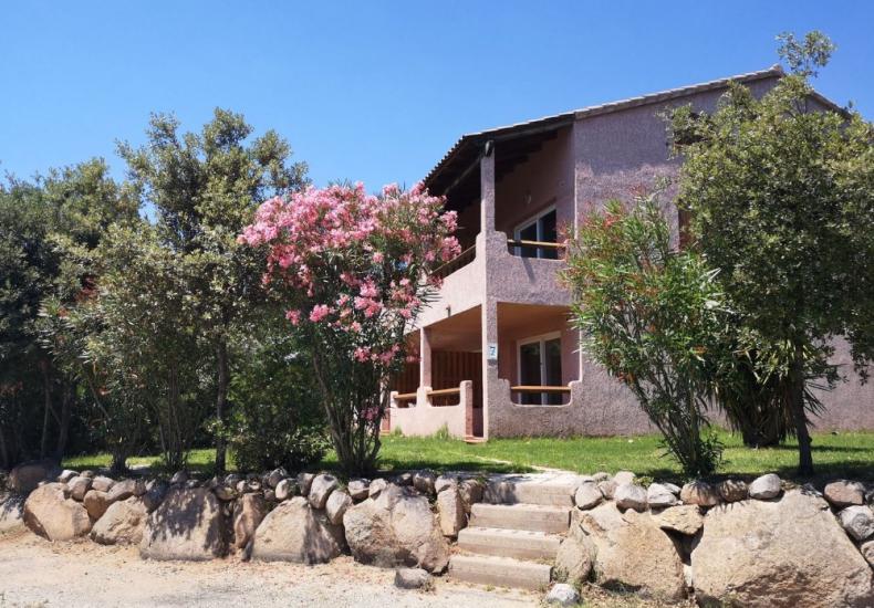 Villa con giardino, fiori rosa e muretto di pietra, sotto un cielo azzurro.