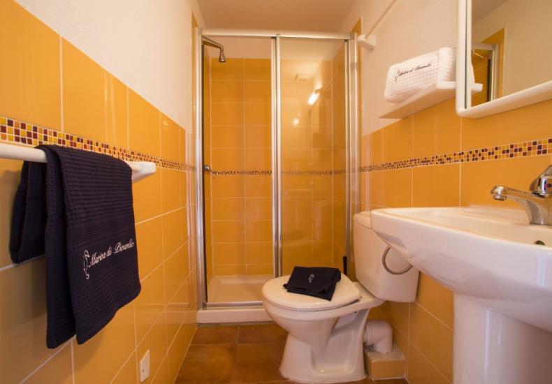 Bagno con doccia, piastrelle arancioni, lavabo e asciugamani scuri.