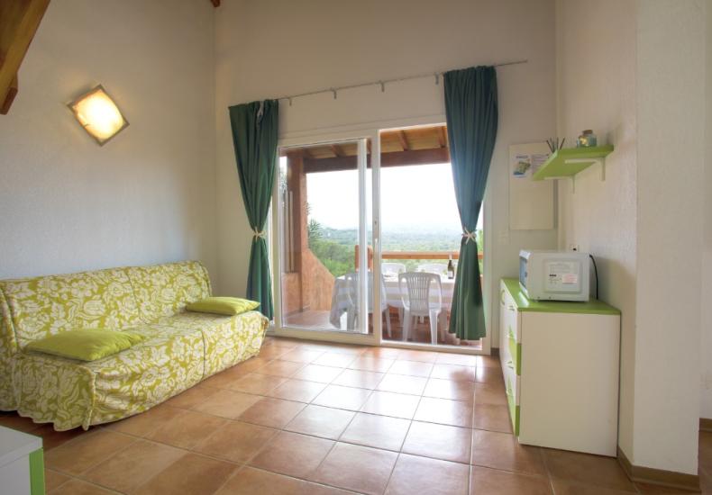 Soggiorno con divano verde, microonde e vista panoramica dal balcone.